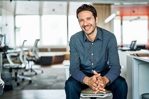 Portrait of confident mid adult businessman. Smiling male professional is sitting with hands clasped. He is in formals at office.